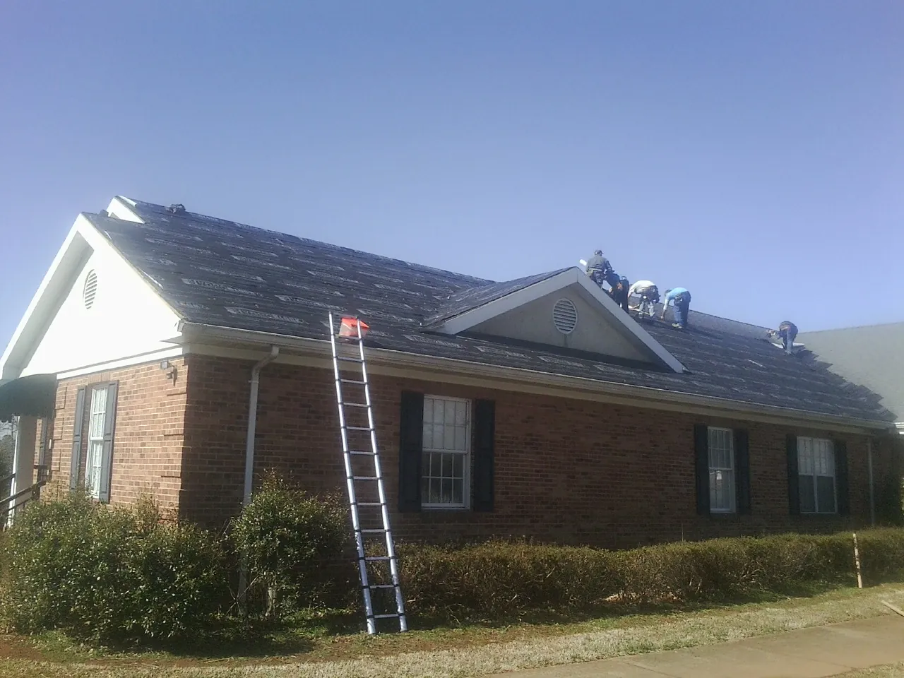 Crew tearing shingles off a brick ranch roof with a ladder set — Emergency Roof Repair work by our crew in Old Saybrook