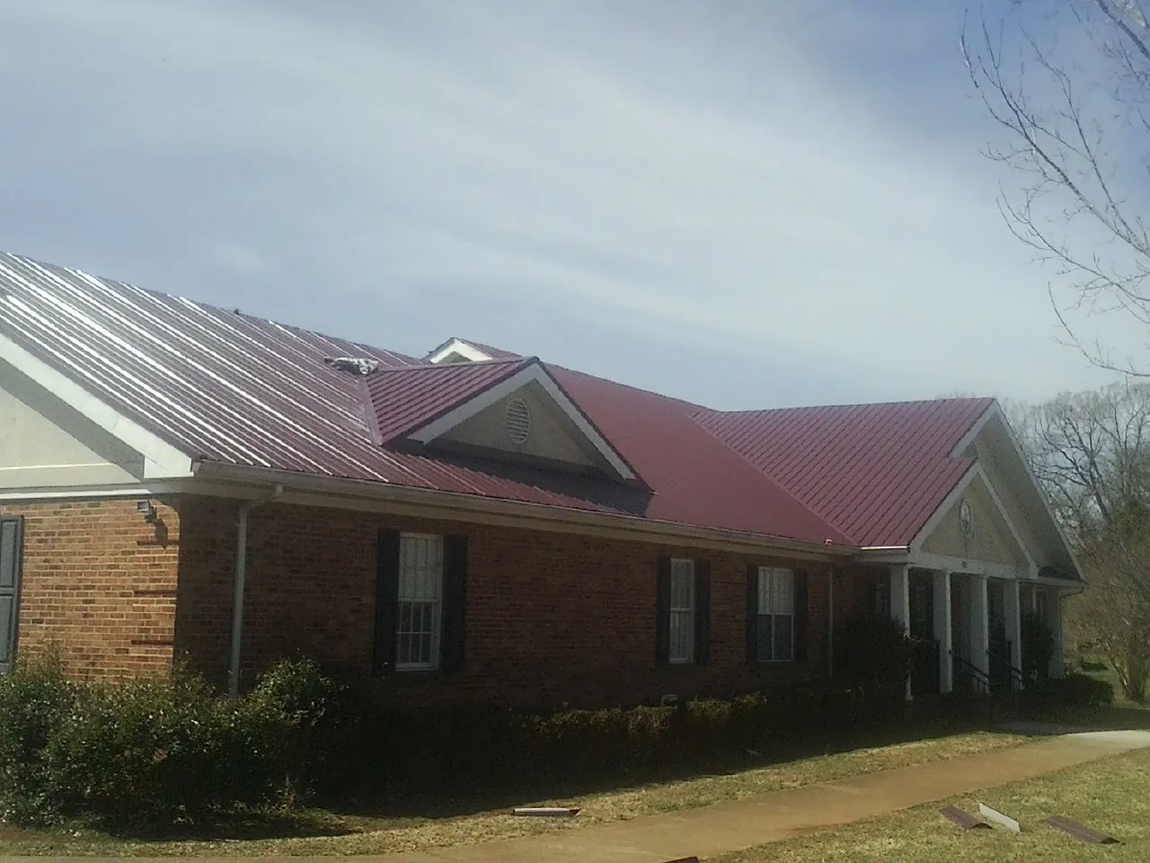 Red metal roof with gabled entries on a long brick building, from a Hail Damage Roof Repair job in Old Saybrook