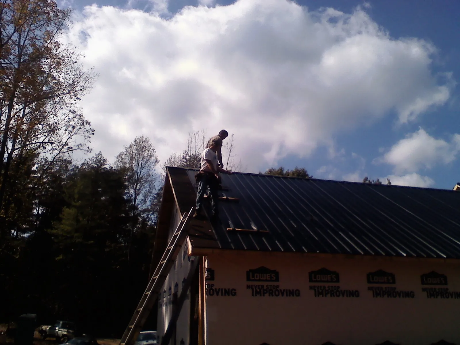 Roofer fastening dark metal panels high against a cloudy sky, from a Roof Inspection job in Old Saybrook